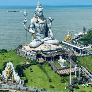 Massive gray Shiva statue overlooking the ocean, with smaller golden and white statues on green hills below from gokarna