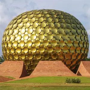 The Matrimandir in Auroville, India, a large golden dome made of many circular discs, with red brick structures from Pondicherry