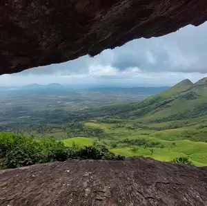 View from a cave opening overlooking a lush green valley with rolling hills under a cloudy sky.